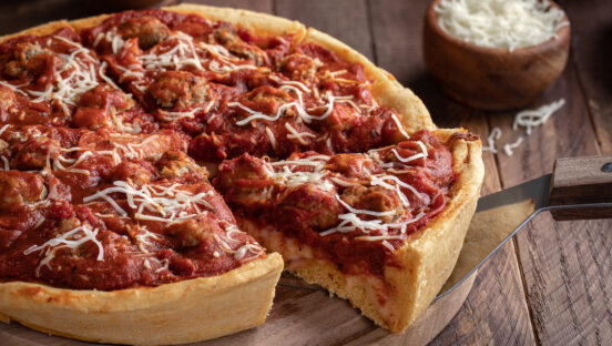 This photo shows a s slice of deep dish sausage pizza on a wooden platter.