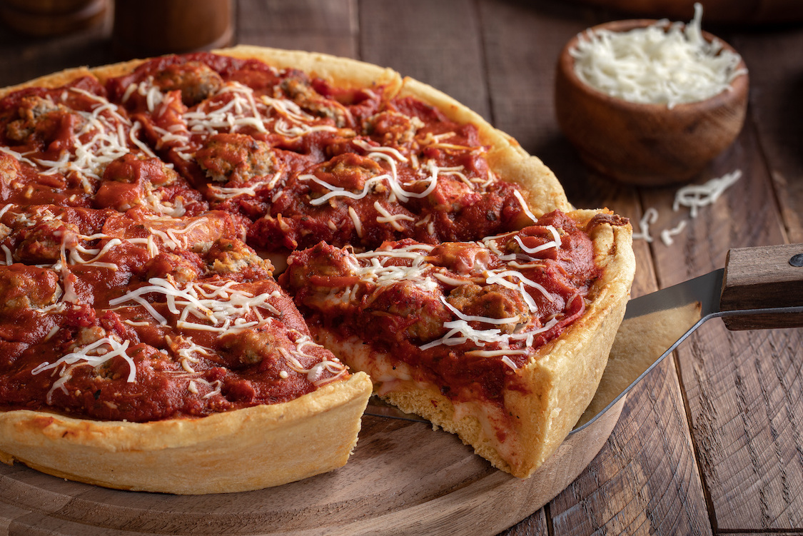 This photo shows a s slice of deep dish sausage pizza on a wooden platter.