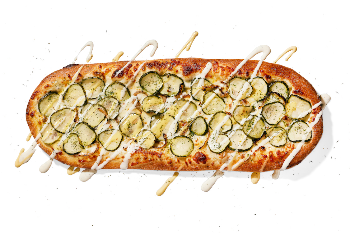 This photo shows a skateboard-shaped pizza topped with lots of pickles and onions.