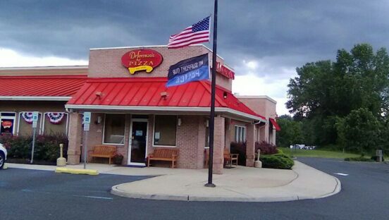 This photo shows the exterior of DeLorenzo's Pizzeria. In front of the building is a U.S. flag and another flag that says, "We Support Our Police."