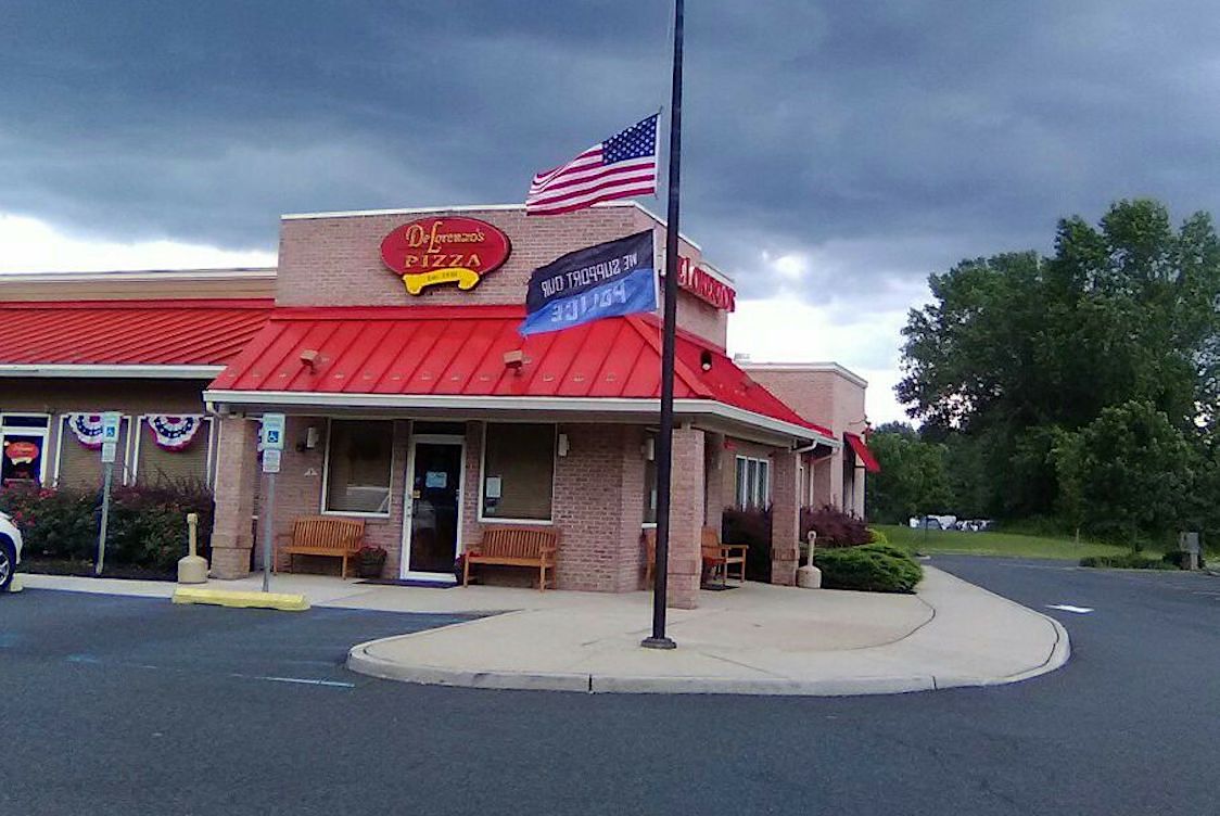 This photo shows the exterior of DeLorenzo's Pizzeria. In front of the building is a U.S. flag and another flag that says, "We Support Our Police."