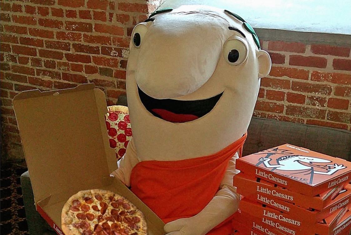 This photo shows someone in the Little Caesars mascot costume holding a pepperoni pizza.