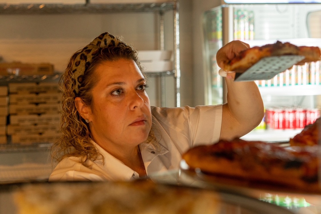 This photo shows Jackie Mazza raising a slice of pizza on a spatula to examine the crispy bottom.