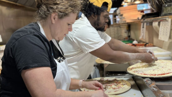 This photo shows Janine Coons working on the pizza-making line with a man working next to her.