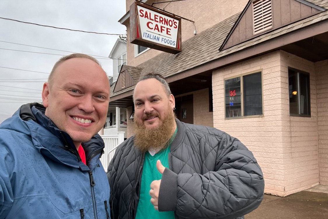 This photo shows Jim Mirabelli and Fernando Greco smiling and posing in front of Salerno's Cafe, with the restaurant's exterior sign in the background.