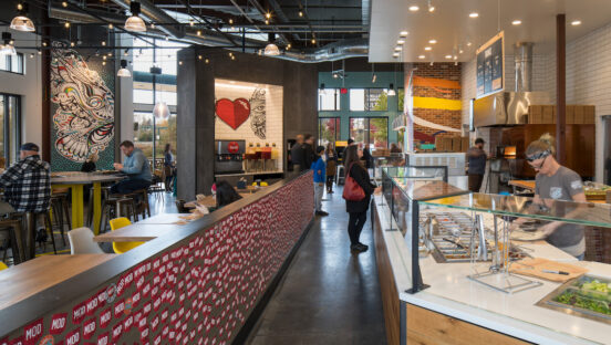 This photo shows the interior of a MOD restaurant with employees making pizzas for customers.