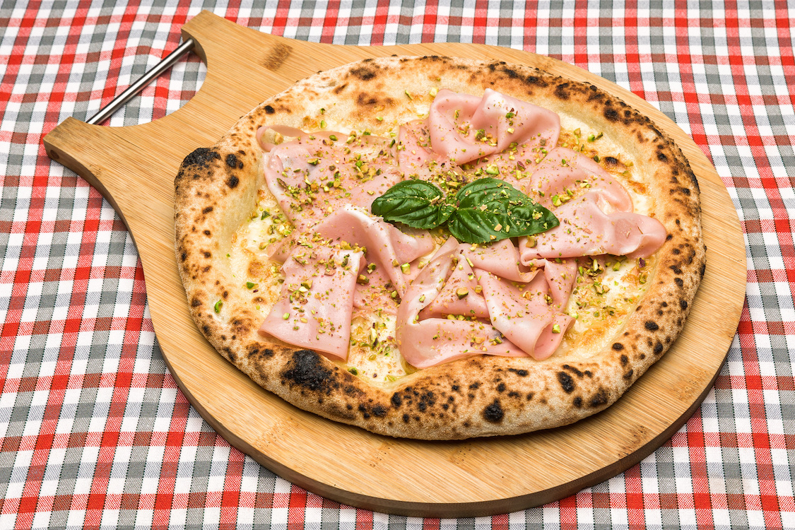This photo shows a pizza with a blistered crust and topped with slices of mortadella.
