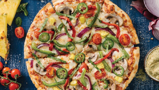This photo shows a pizza topped with green peppers, jalapeño slices, fresh basil, red onions and cherry tomatoes.