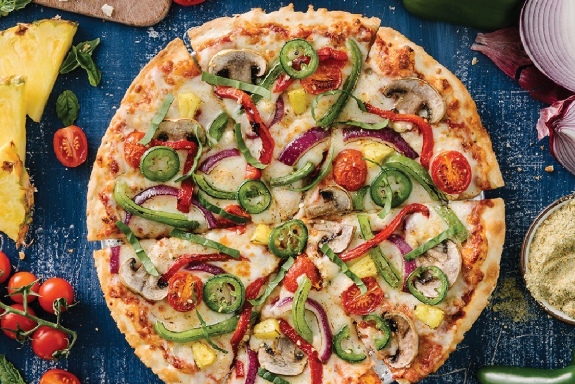 This photo shows a pizza topped with green peppers, jalapeño slices, fresh basil, red onions and cherry tomatoes.