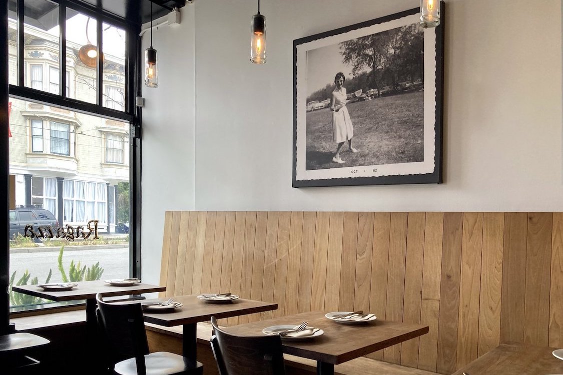 This photo of Ragazza's dining room shows a pair of tables with a vintage black-and-white photo of a female member of Sharon Ardiana's family above, next to a window offering a view outside the restaurant.