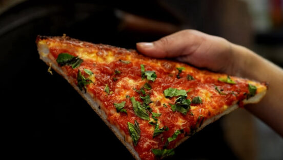 This photo shows a man's hand holding a slice of the Skinny Deep Dish pizza with cheese, sauce and shredded basil.