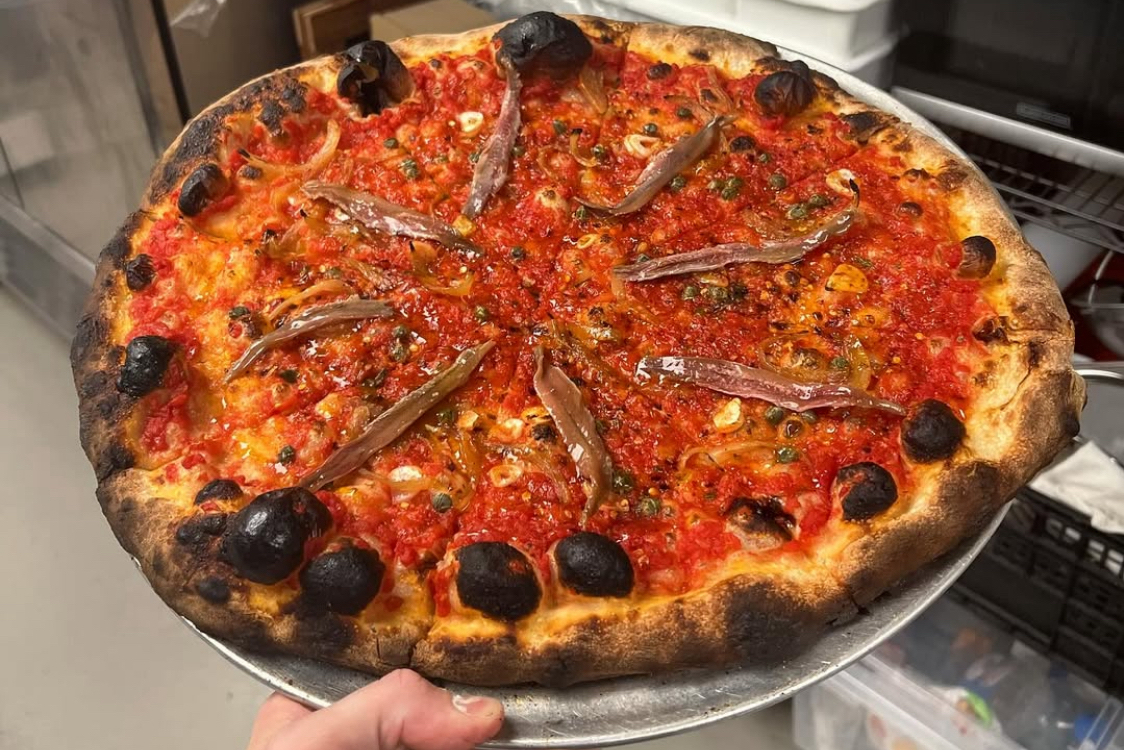 This photo shows a pizza with a beautifully blistered crust topped with anchovies and black olives.