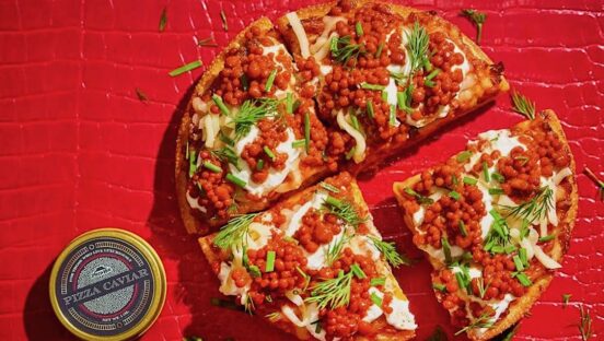 This photo shows a pizza topped with reddish pepperoni-flavored pearls, cheese, green onions and parsley.