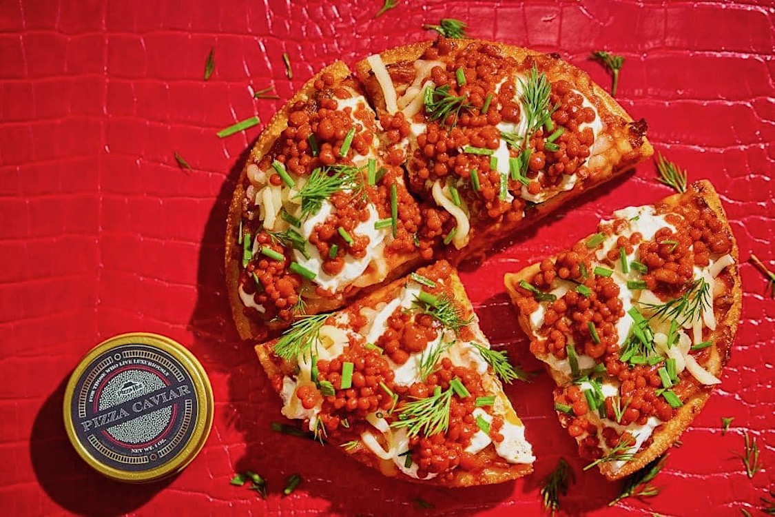 This photo shows a pizza topped with reddish pepperoni-flavored pearls, cheese, green onions and parsley.