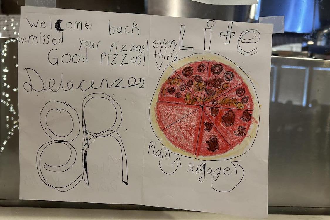 This photo shows a child's handwritten note welcoming DeLorenzo's Pizza back, along with a drawing of a sausage pizza.