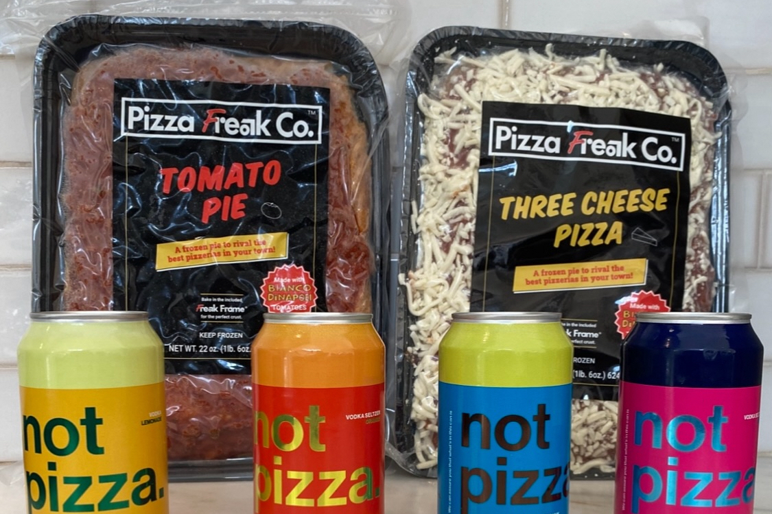 This photo shows Pizza Freak Co.'s packaged Three Cheese Pizza and Tomato Pie with several canned beverages lined up in front of them.