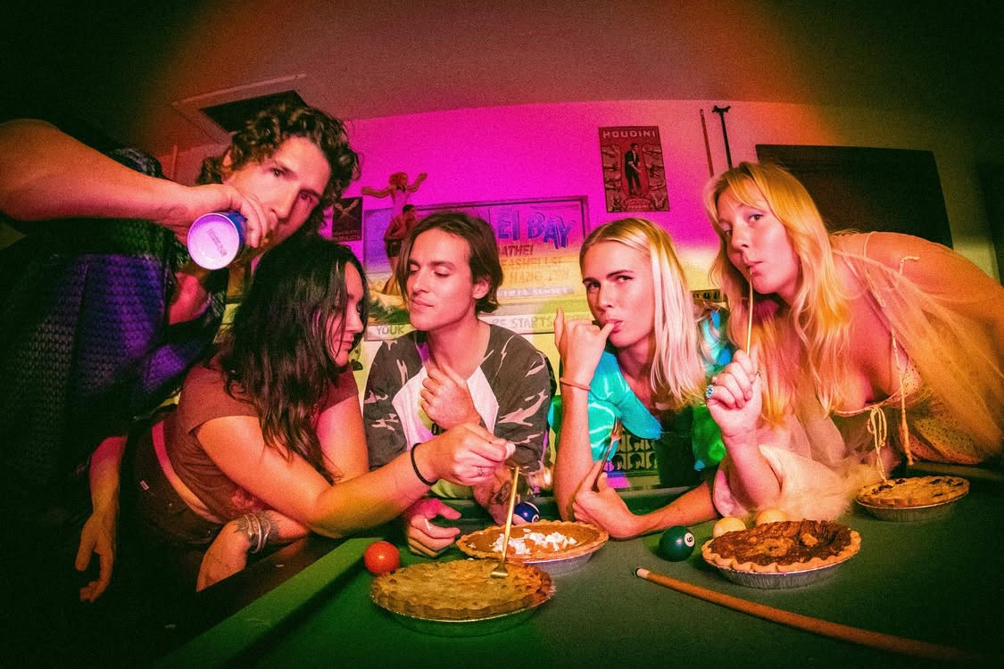 This photo shows a group of hip young people, bunched together at a table and eating pumpkin pies.