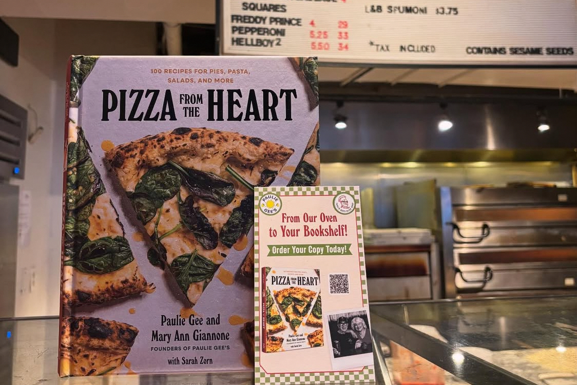 This photo shows a copy of "Pizza From the Heart" and signage promoting the book on the counter at Paulie Gee's Soul City Slice.