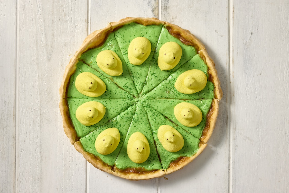 This photo shows a pizza topped with green sugar crystals and a bunch of yellow Peeps in a circle.