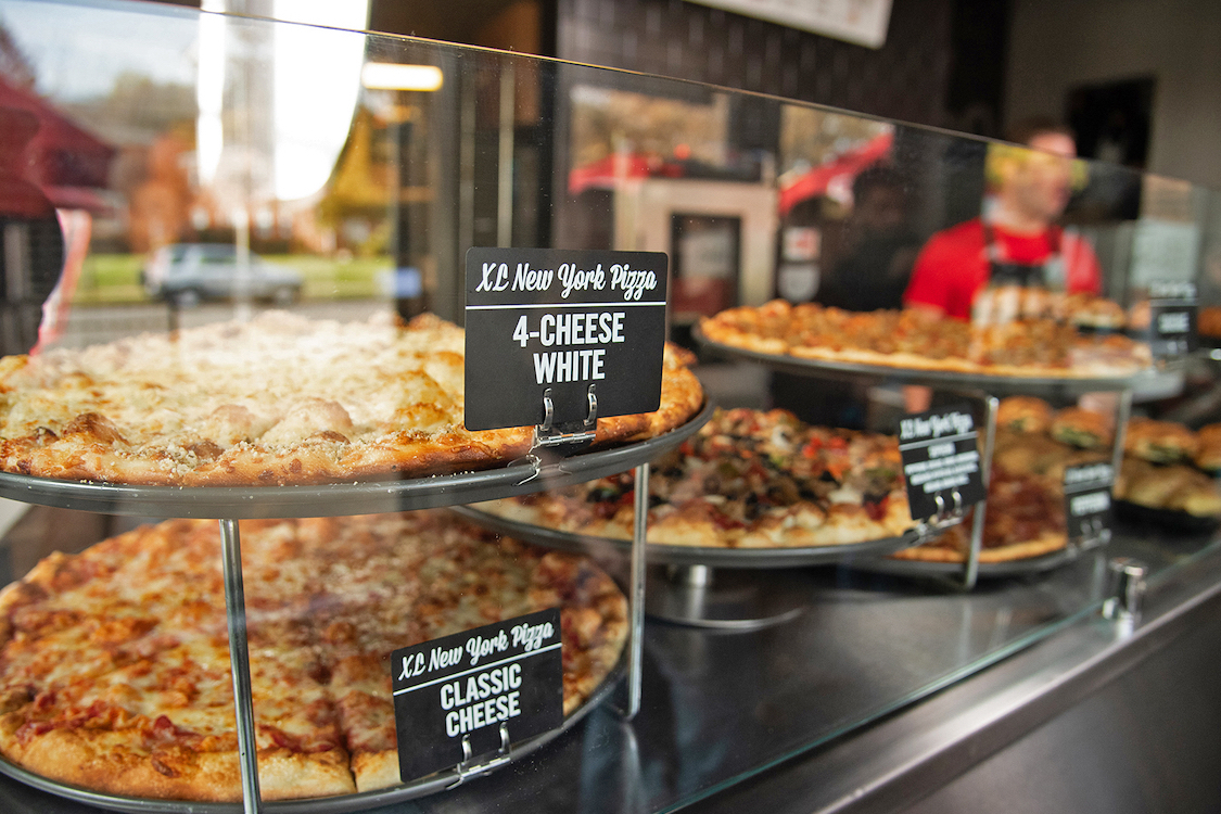This photo shows a display of multiple pizzas, including a 4-Cheese and a Classic Cheese, at a Sbarro location.