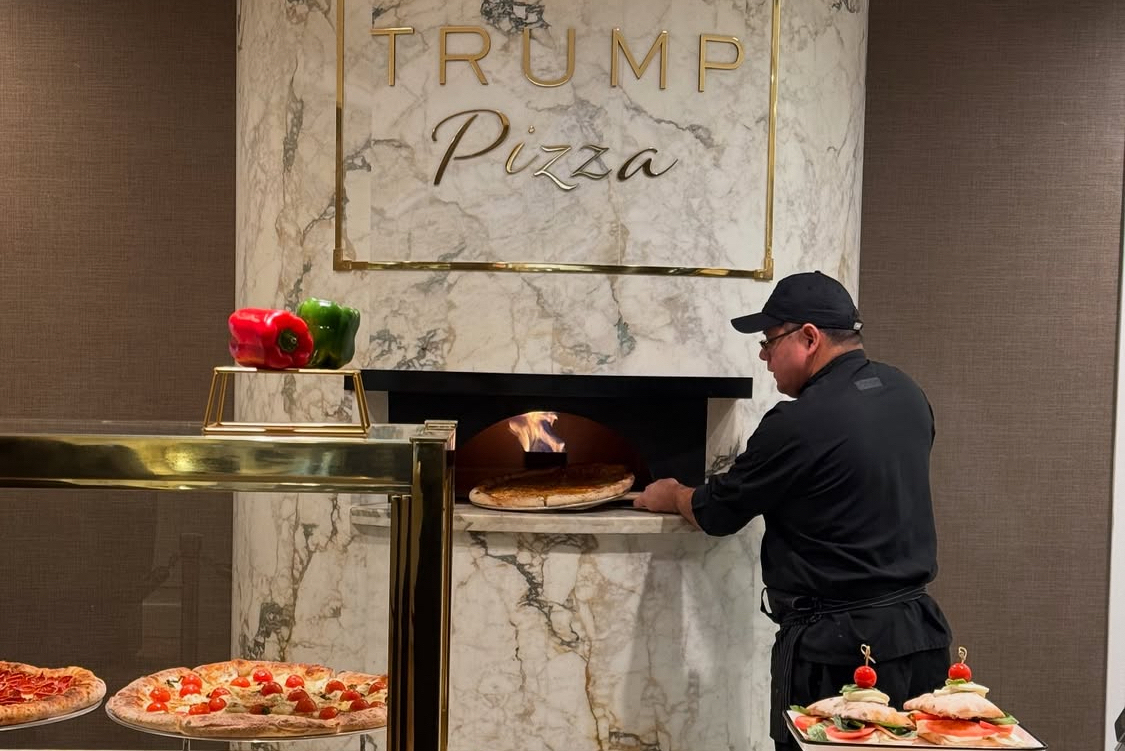 This photo shows a man, dressed all in black, peeling a pizza into a Trump Pizza oven at Trump Tower in New York.