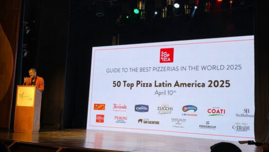 This photo shows a man standing at a podium on stage at 50 Top Pizza's awards presentation. Behind him is a huge screen with the words, "50 Top Pizza Latin America 2025"