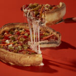 This photo shows a slice being removed from a whole Italian Beef Pizza with a nice cheese pull.