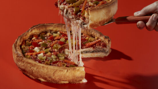 This photo shows a slice being removed from a whole Italian Beef Pizza with a nice cheese pull.