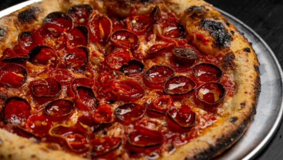 This photo shows a pizza with a beautifully blistered crust topped with pepperoni and Fresno chilis.