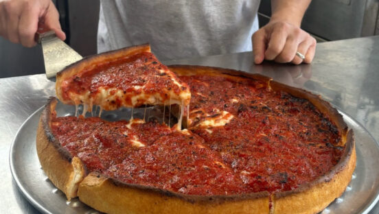 This photo shows a man's hand pulling out a slice of deep-dish pizza with a spatula.