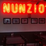 This photo shows a bright yellow and red neon sign that says Nunzio's from the pizzeria.