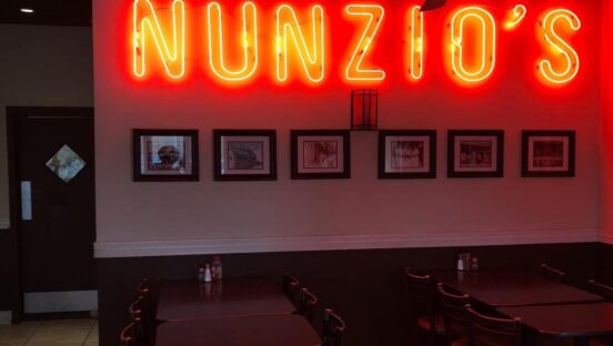 This photo shows a bright yellow and red neon sign that says Nunzio's from the pizzeria.