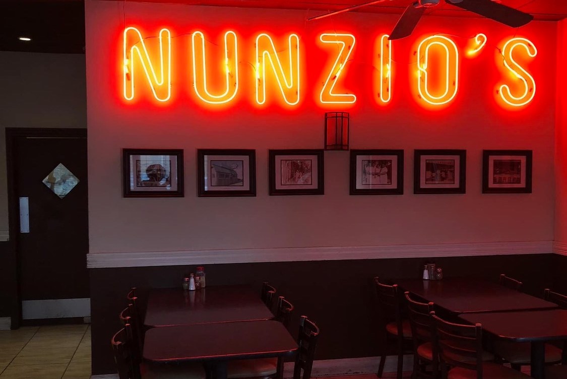 This photo shows a bright yellow and red neon sign that says Nunzio's from the pizzeria.