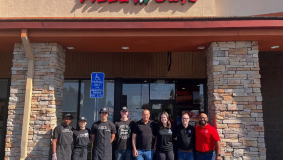 This photo shows a group of owners and employees standing in front of a new Pizza Guys location.