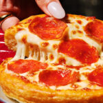 This photo shows a woman's fingers pulling a slice from a personal pan pizza topped with pepperoni.