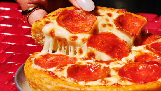 This photo shows a woman's fingers pulling a slice from a personal pan pizza topped with pepperoni.