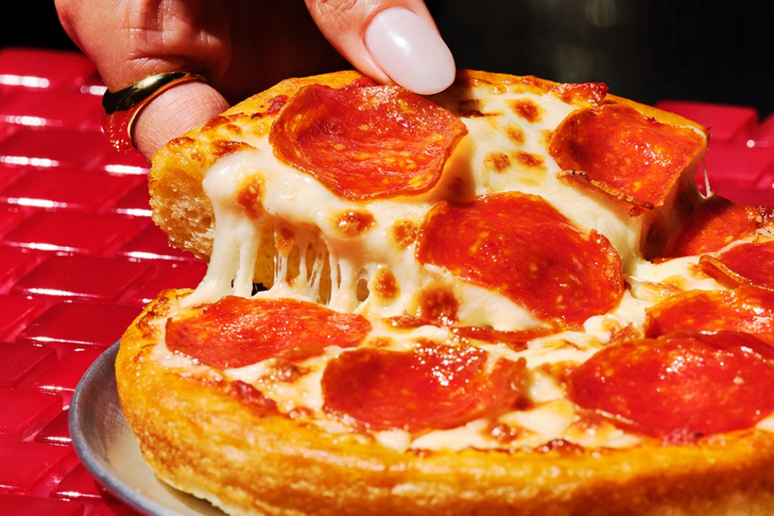 This photo shows a woman's fingers pulling a slice from a personal pan pizza topped with pepperoni.