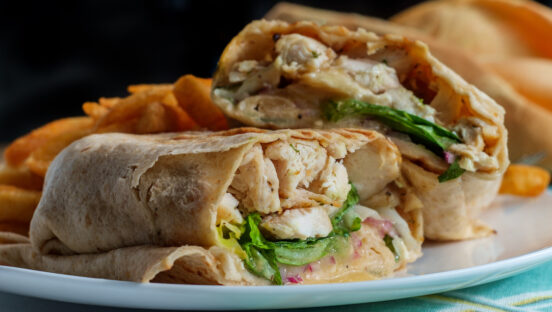 This photo shows a Chicken Caesar salad wrap sandwich with romaine lettuce and French fries.