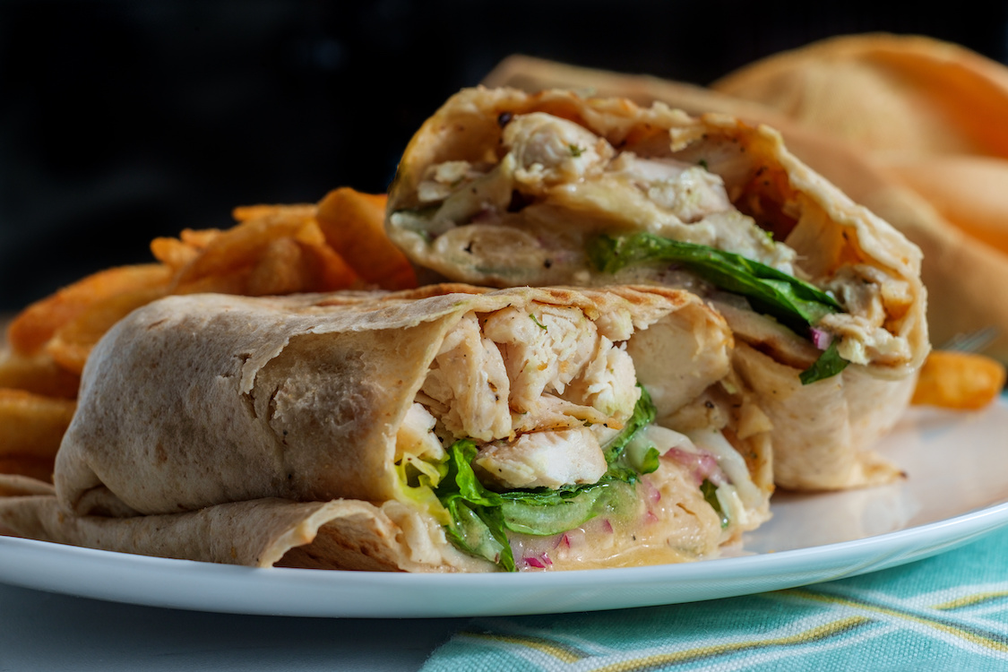 This photo shows a Chicken Caesar salad wrap sandwich with romaine lettuce and French fries.
