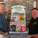 This photo shows Scott Van Duzer and a local police officer posing with a set of books in a display case in his pizzeria.