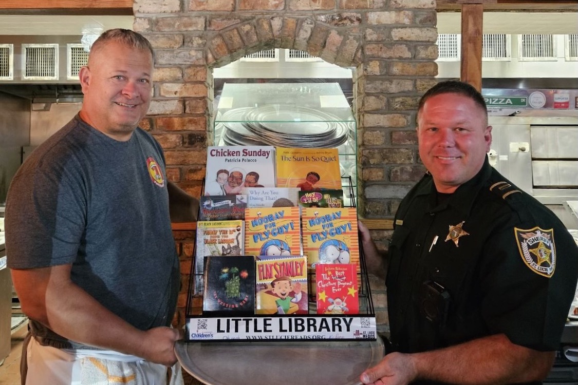 This photo shows Scott Van Duzer and a local police officer posing with a set of books in a display case in his pizzeria.