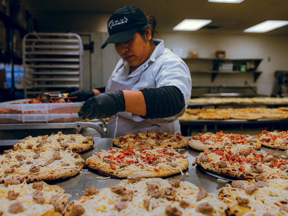 A woman tops pizzas in a frozen pizza factory
