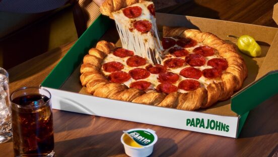 This photo shows a person's hand removing a slice from the croissant pizza with a nice cheese pull.