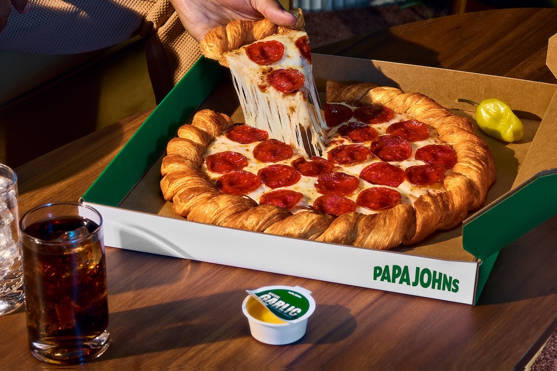 This photo shows a person's hand removing a slice from the croissant pizza with a nice cheese pull.