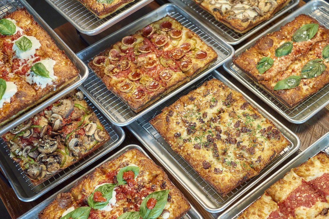 This photo shows a wide variety of Detroit-style pizzas offered by Emmy Squared Pizza.