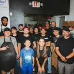 This photo shows NBA player Julian Champagnie posing with the staff at 550 Pizzeria, with Janet Zapata in front.