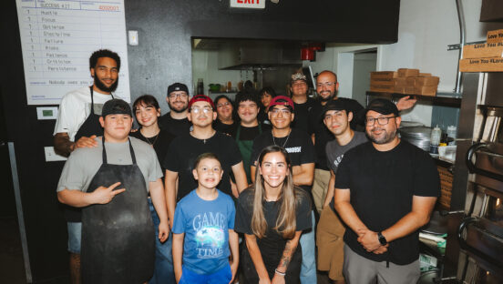 This photo shows NBA player Julian Champagnie posing with the staff at 550 Pizzeria, with Janet Zapata in front.