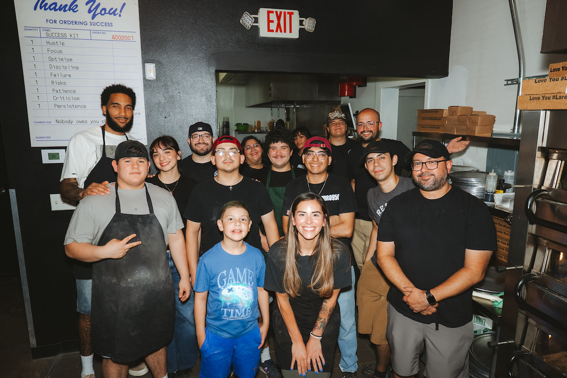 This photo shows NBA player Julian Champagnie posing with the staff at 550 Pizzeria, with Janet Zapata in front.