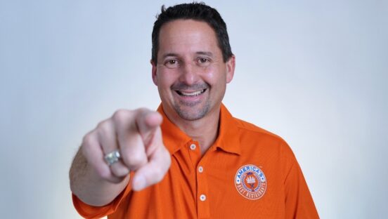 This photo shows Matt Plapp in an orange shirt smiling and pointing confidently at the camera.