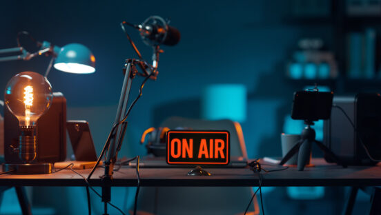 This photo shows a podcast studio desk with microphones and a sign that says "On Air" in red letters.